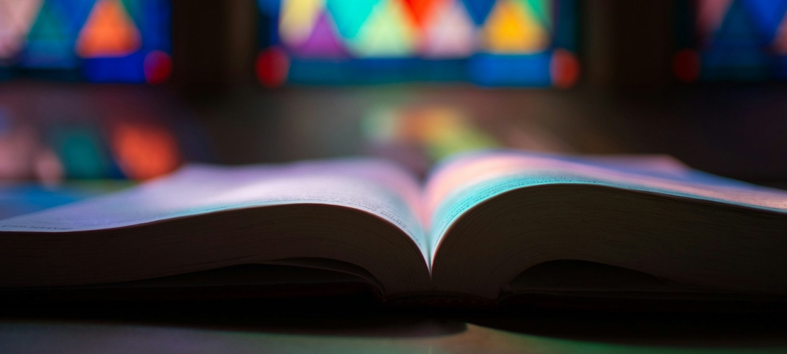 Aufgeschlagenes Buch vor einem bunten Kirchenfenster